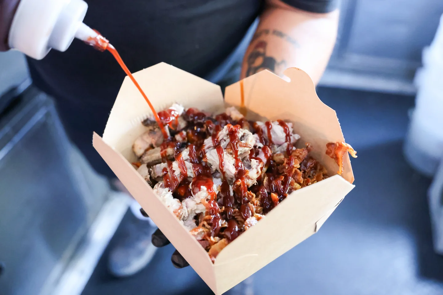 BBQ sauce being squeezed over a loaded pulled pork box