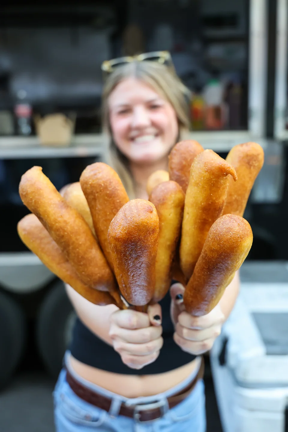 Woman holding corndogs on sticks outside The Gravy Train, wider shot