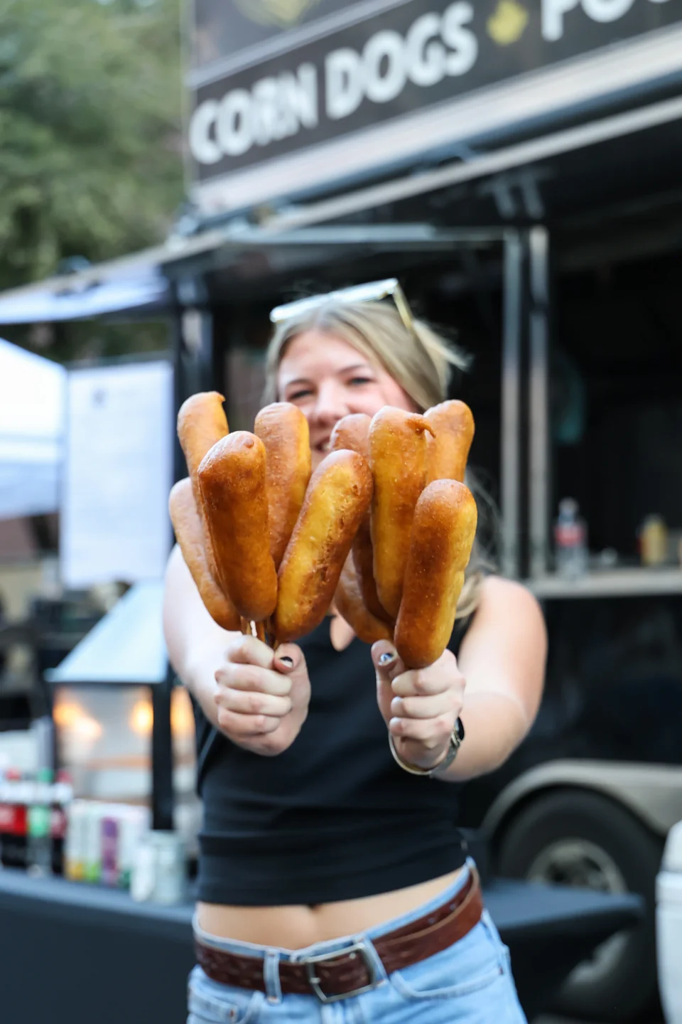 Woman holding corndogs in front of Corn Dogs Poutine truck sign at night