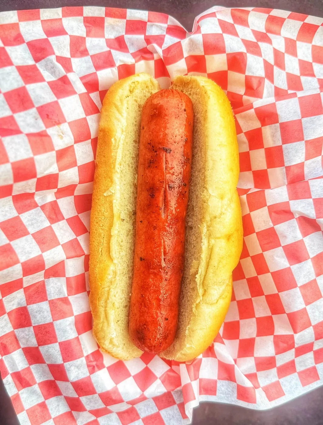 Grilled hot dog in a bun on checkered paper