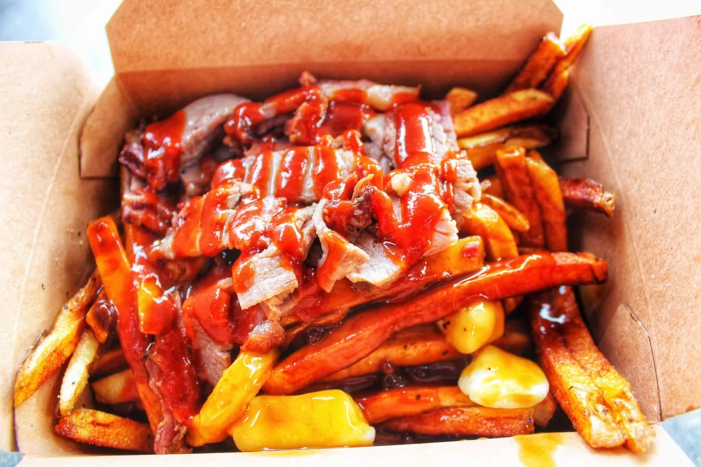 Brisket poutine in a takeout box, topped with BBQ sauce and cheese curds