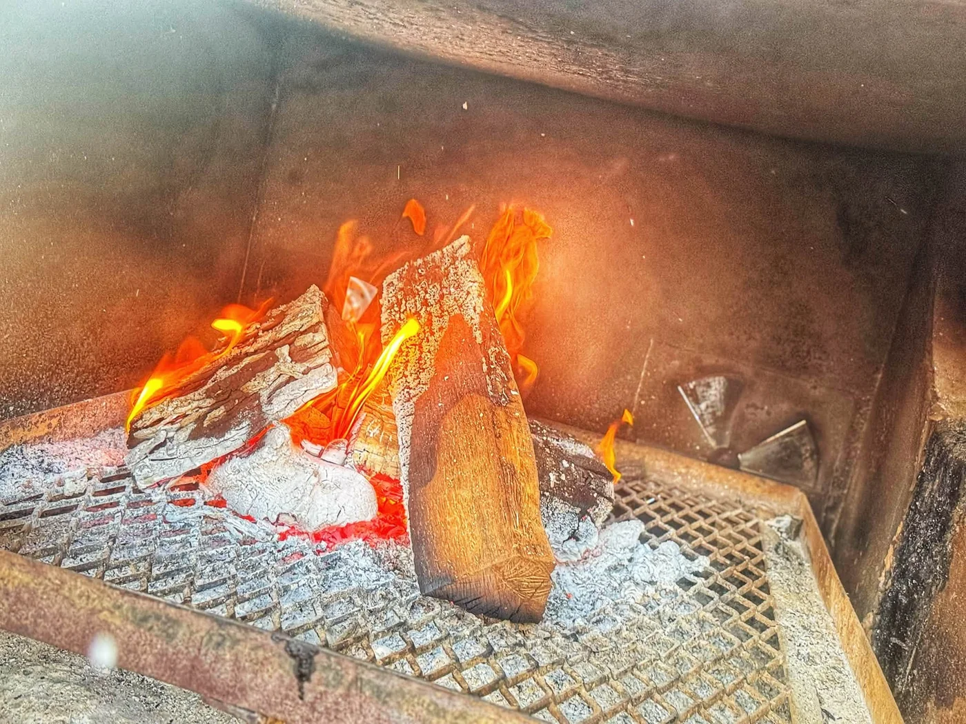 Wood logs burning over hot coals in the smoker
